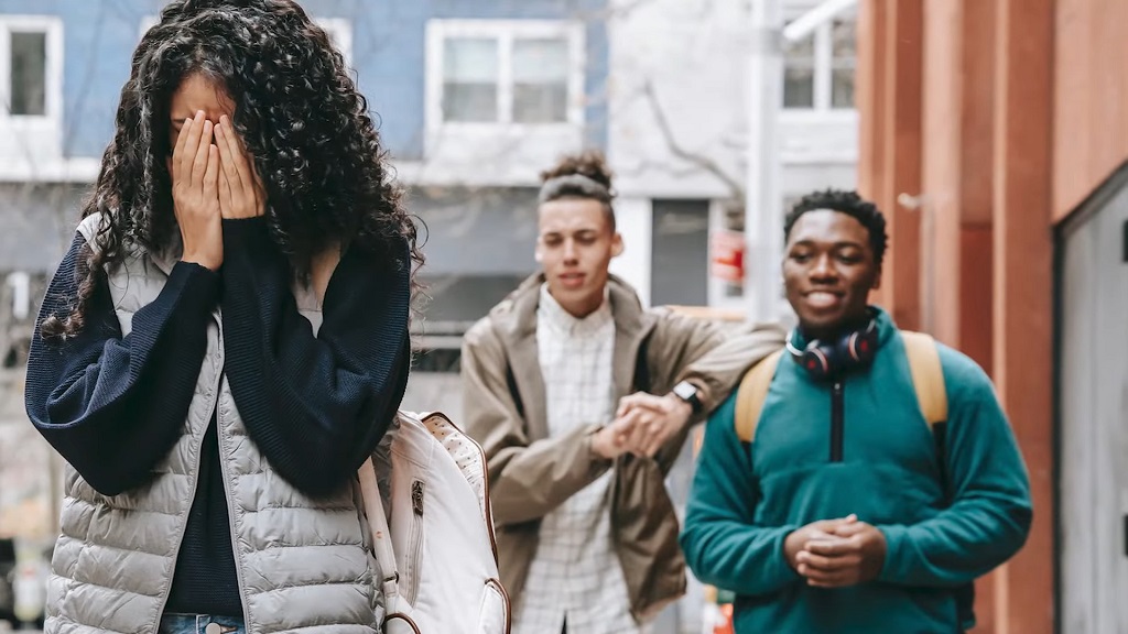 A young girl covers her face while two young men stand behind her