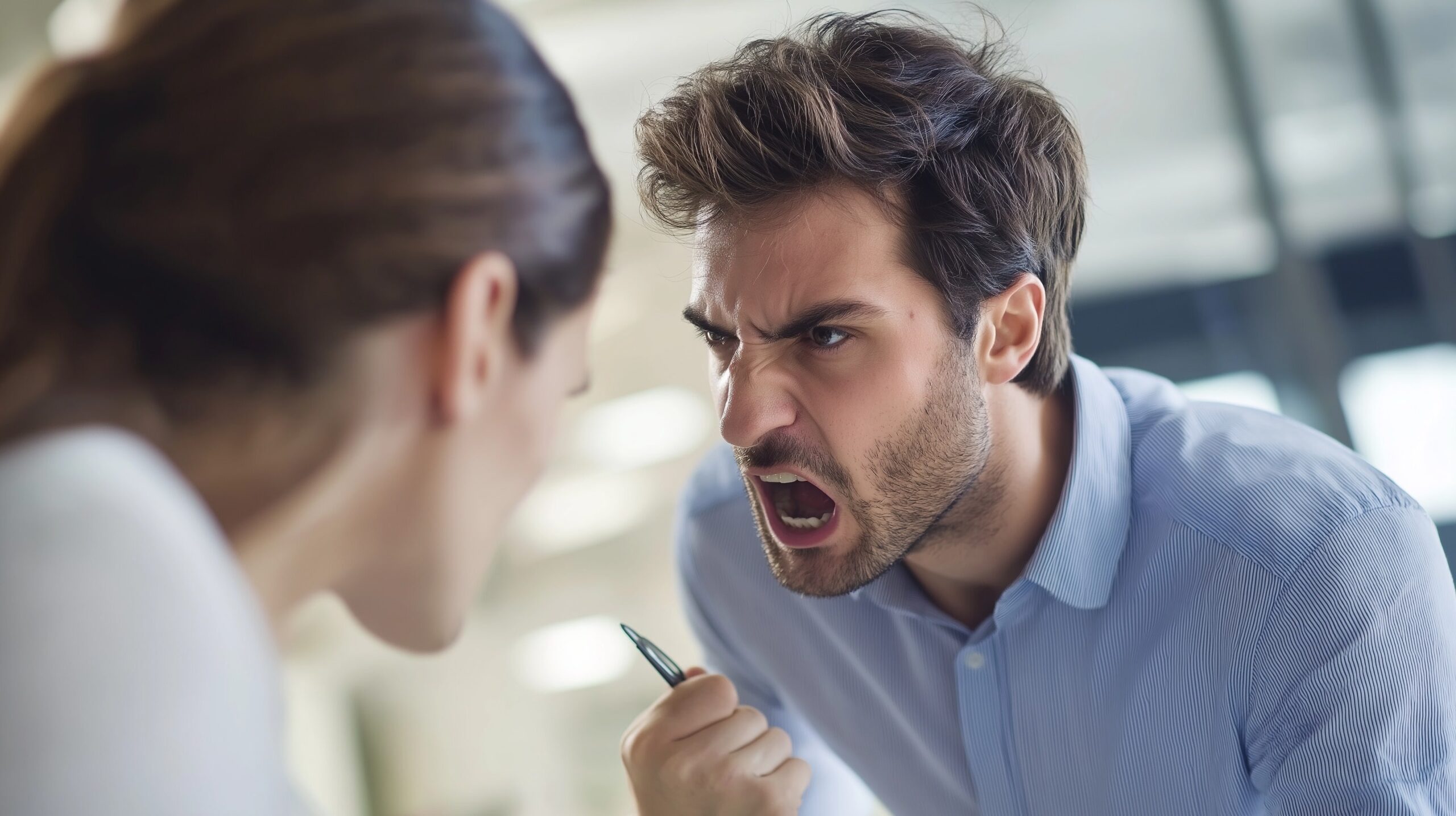 A man angrily yelling at a woman in a professional setting, displaying workplace aggression