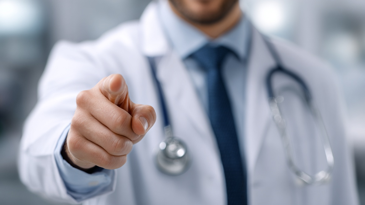 Doctor in a white coat pointing forward with a stethoscope around the neck in a clinical setting